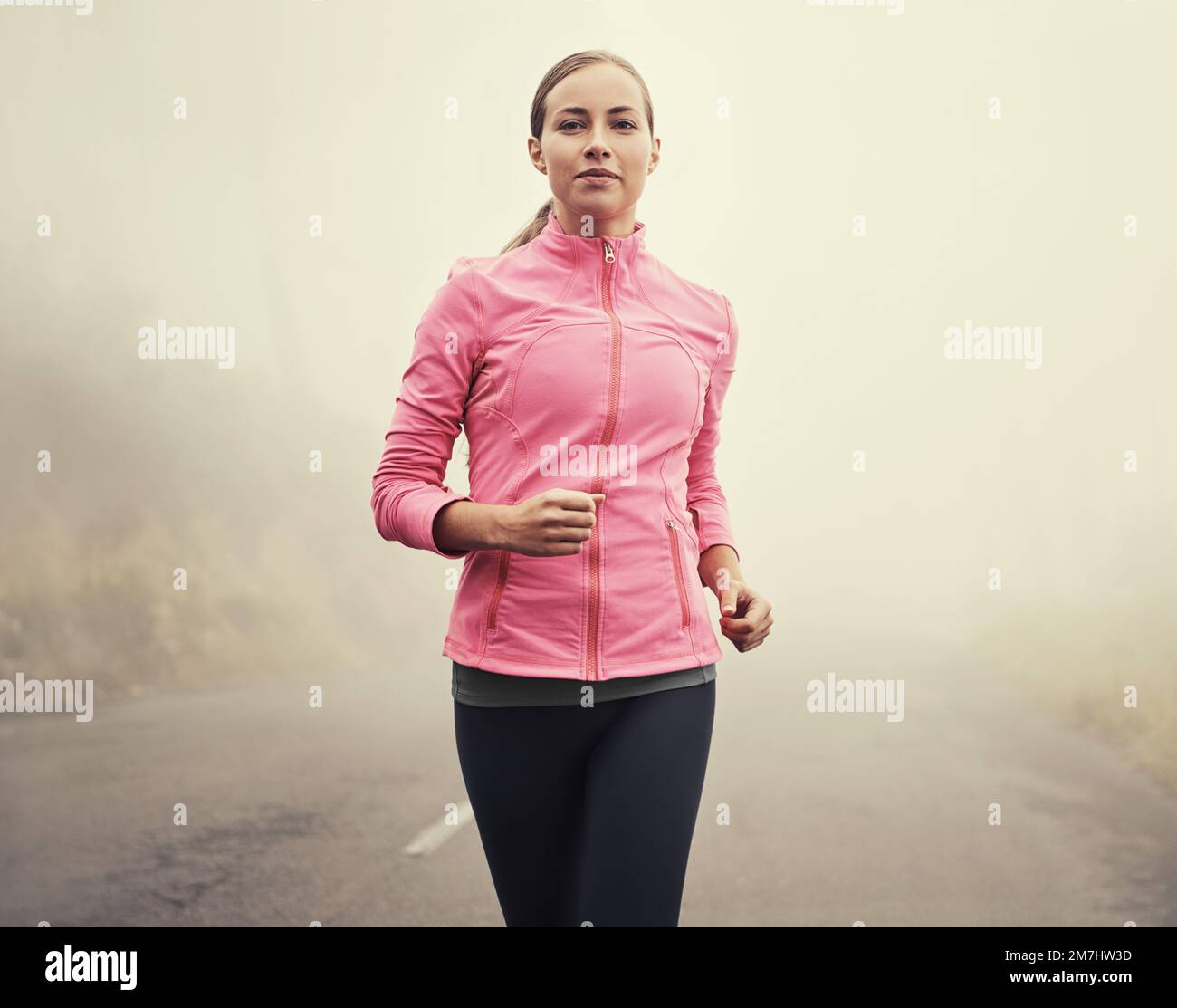 Purer Genuss auf freier Straße. Eine junge Frau, die an einem nebligen Morgen auf einer Landstraße joggt. Stockfoto