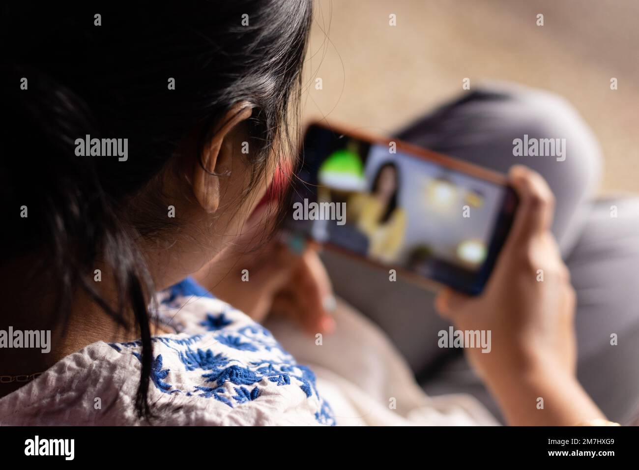 Eine indische Frau mit Smartphone, die zu Hause OTT-Anwendungen genießt Stockfoto