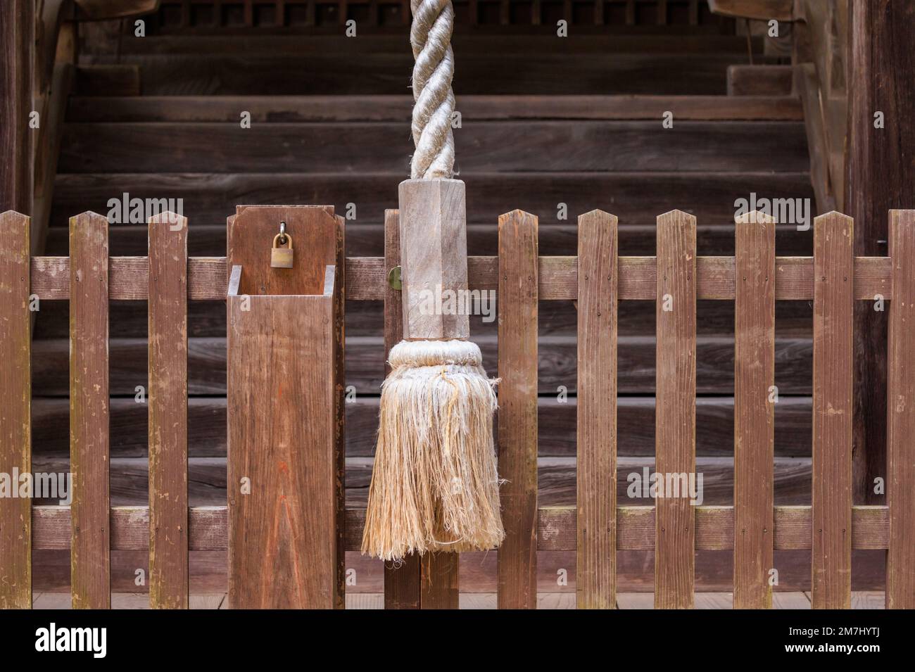 Großes Seil zum Klingeln am japanischen Tempel und kleines Vorhängeschloss auf Holzzaun Stockfoto