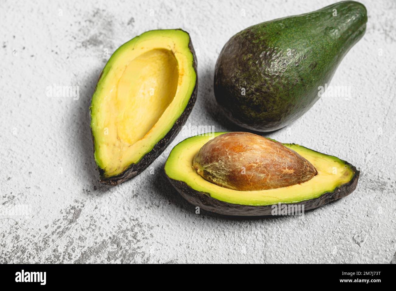 Draufsicht sowohl von geschnittener als auch von ganzer reifer Avocado auf einem Tisch aus weißem Stein Stockfoto