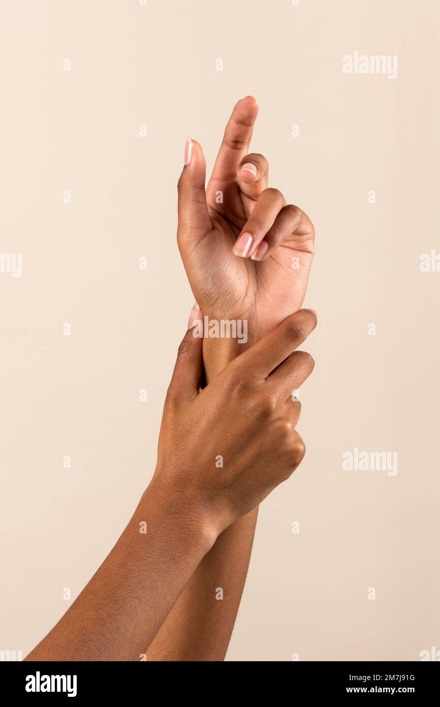 Hände einer afroamerikanischen Frau, die sich das Handgelenk berührt und eine perfekte Maniküre vor beigefarbenem Hintergrund zeigt Stockfoto