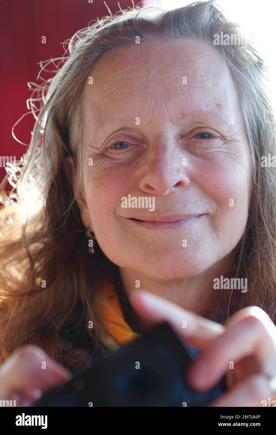 Eine freundliche 63-jährige Frau ohne Make-up mit einer Kamera in der Hand schaut in die Kamera Stockfoto