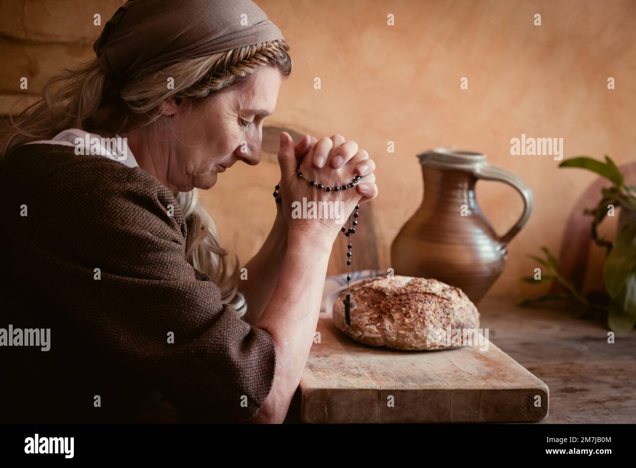 Frau im authentischen bäuerlichen Renaissance-Kostüm, die an einem Tisch betet. Es gibt Brot auf dem Tisch. Stockfoto