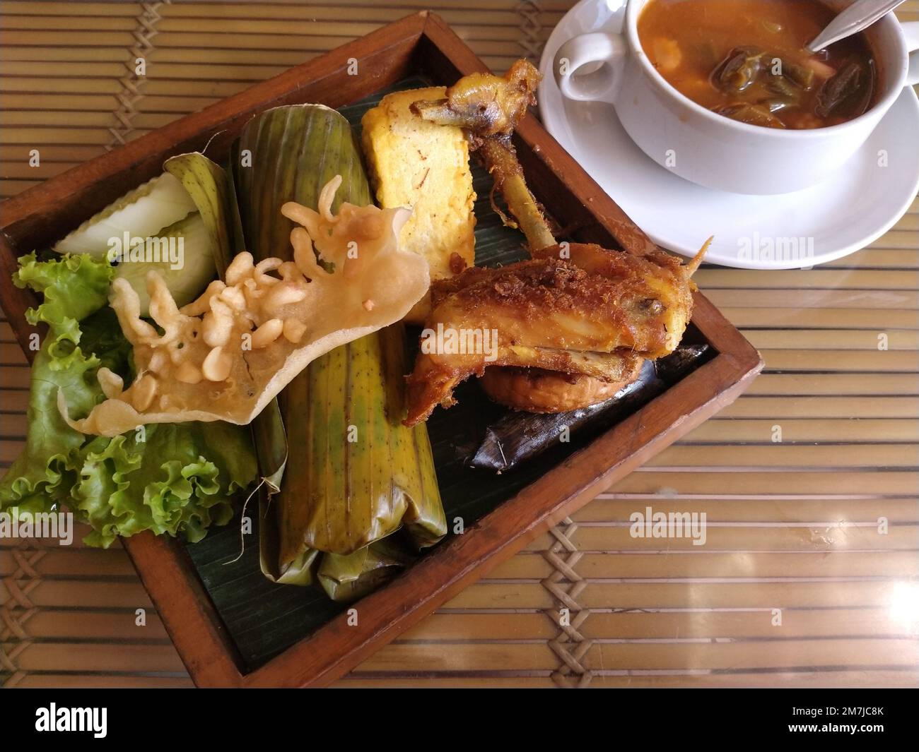 Köstliche indonesische Mahlzeit Nasi bakar auf Bananenblatt. Komplettes Set mit gebratenem Hähnchen, frischem Gemüse und saurer Suppe Stockfoto