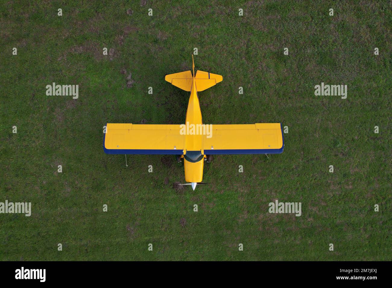 Kleines gelbes Flugzeug, das für Kurzstreckenflüge von oben gesehen wird und auf einem grünen Feld geparkt ist Stockfoto