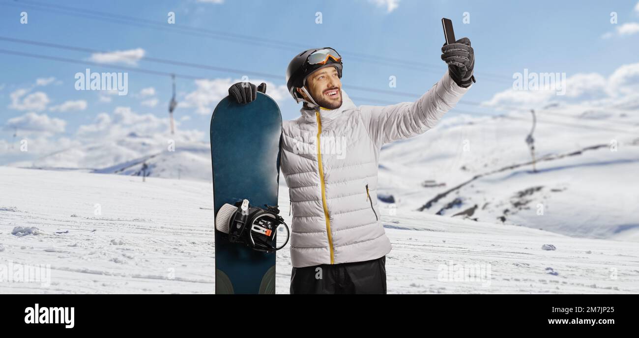 Ein Mann mit einem Snowboard macht ein Selfie mit einem Smartphone auf einem verschneiten Berg Stockfoto