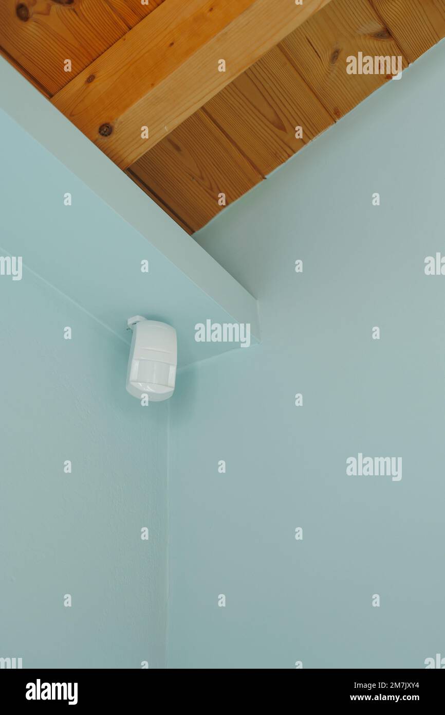Bewegungsmelder oder Melder für Sicherheitssystem an blauer Wand in Mansarde mit Holzdecke montiert. Stockfoto