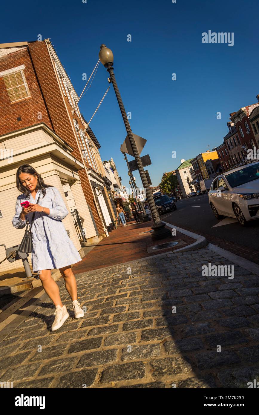 Eine Frau, die auf ihr Telefon schaut, ist die angesagte, gehobene Wisconsin Avenue mit schicken Geschäften und Restaurants in Georgetown, einem historischen Viertel, und Kommerzen Stockfoto