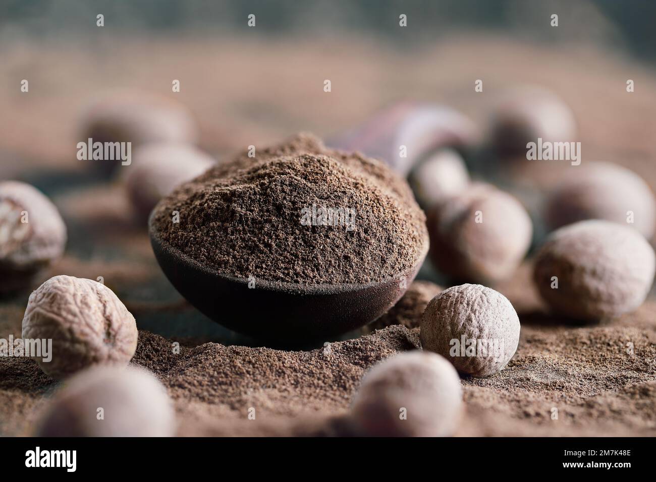 Getrockneter Muskatnuss in einem Holzlöffel, mit ganzer Muskatnuss in der Nähe. Selektiver Fokus mit extrem verschwommenem Vorder- und Hintergrund. Stockfoto