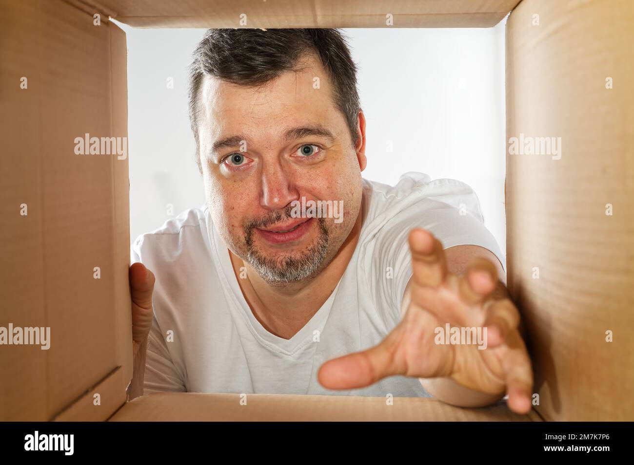 Glücklicher Mann, der auspackt, den Karton öffnet und reinschaut. Ein lächelnder Mann beim Auspacken und eine Schachtel Stockfoto