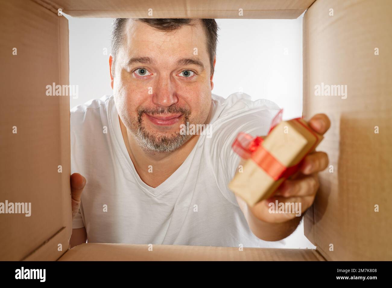 Glücklicher Mann, der auspackt, den Karton öffnet und reinschaut. Ein lächelnder Mann beim Auspacken und eine Schachtel Stockfoto