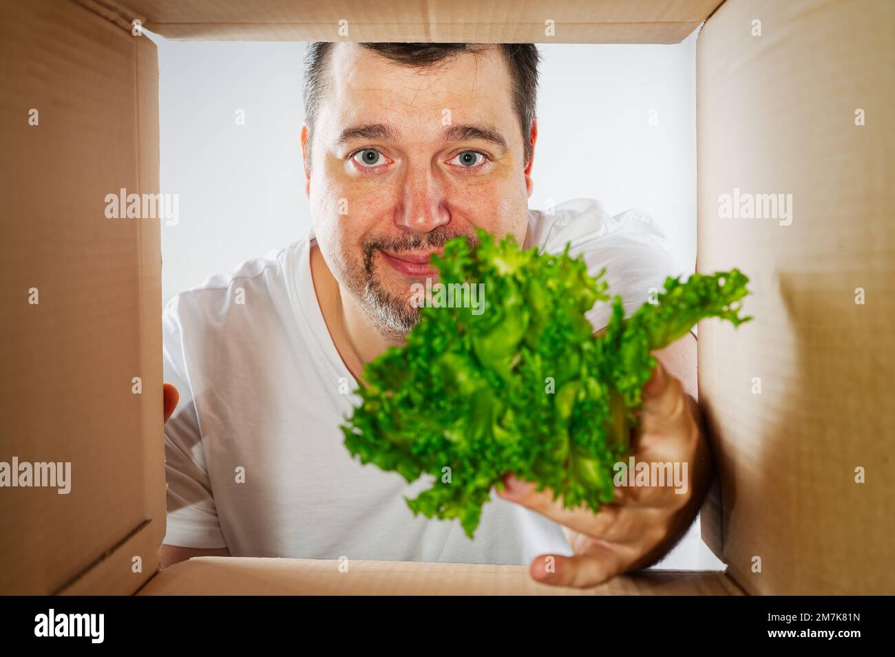 Glücklicher Mann, der auspackt, den Karton öffnet und reinschaut. Ein lächelnder Mann beim Auspacken und eine Schachtel Stockfoto