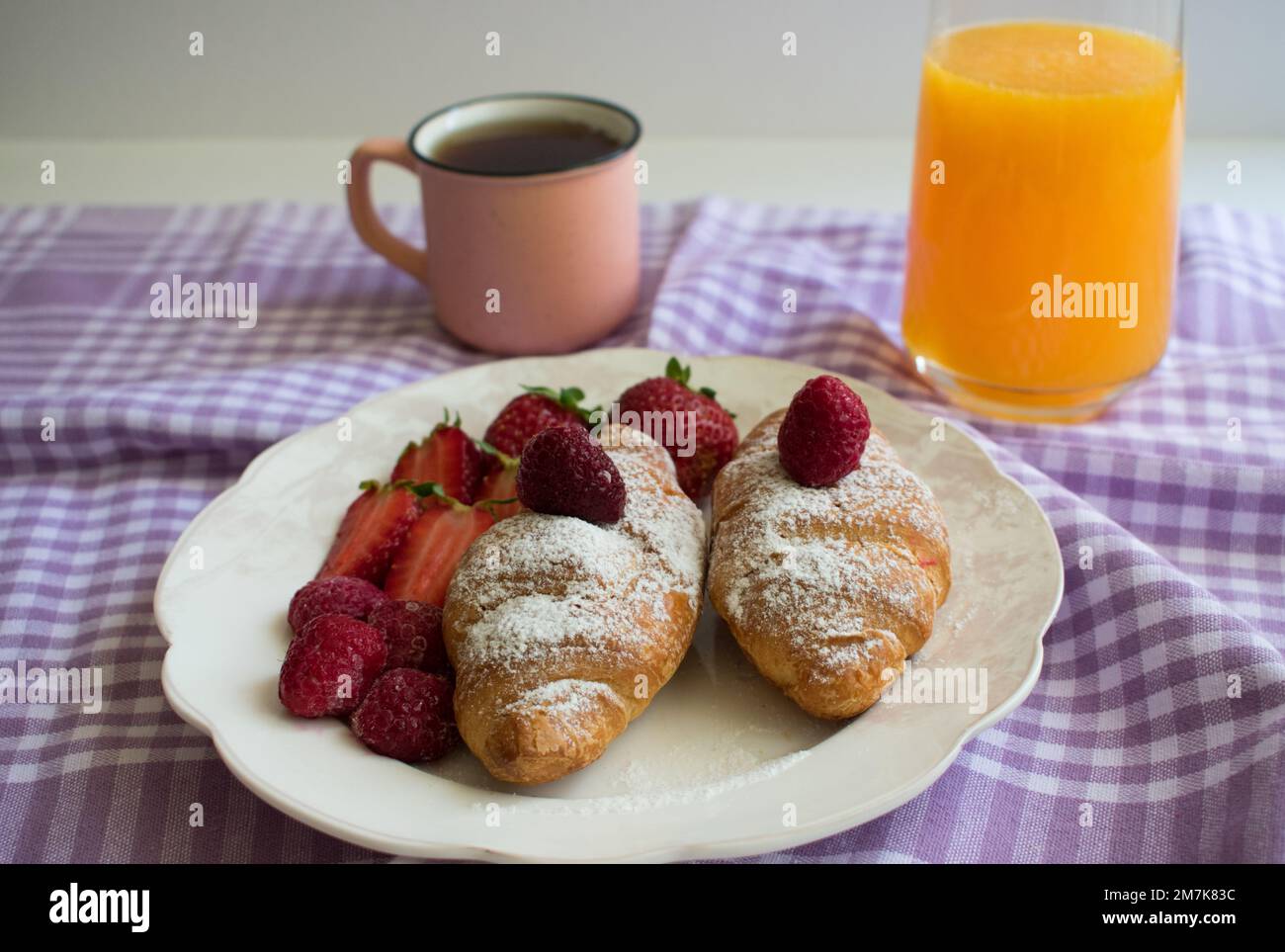 Frisches Croissant auf weißem Teller, serviert mit Erdbeere, Himbeere, Orangensaft und Tee. Stockfoto