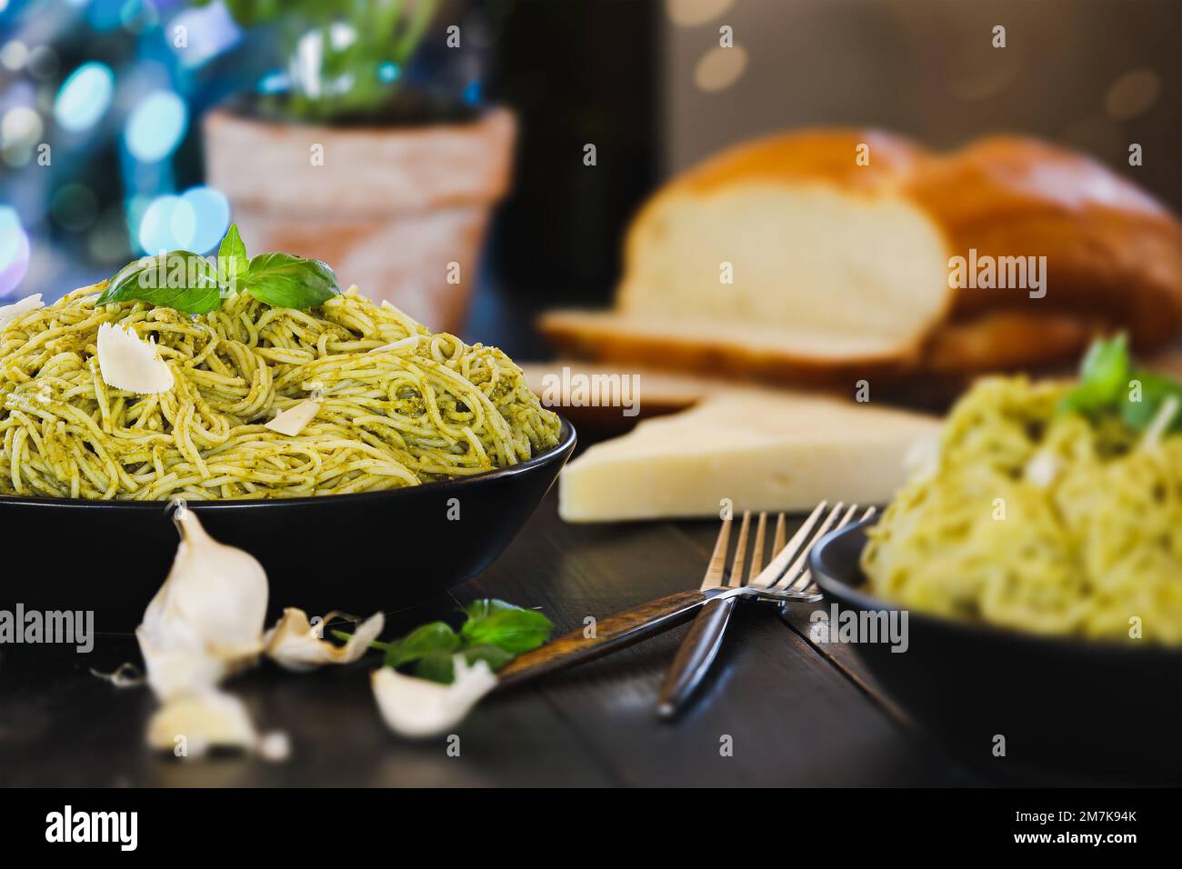 Selektiver Fokus auf zwei Platten Pesto-Spaghetti-Pasta mit frischen Basilikumblättern und Parmesan-Käse auf einem schwarzen rustikalen Holztisch. Stockfoto