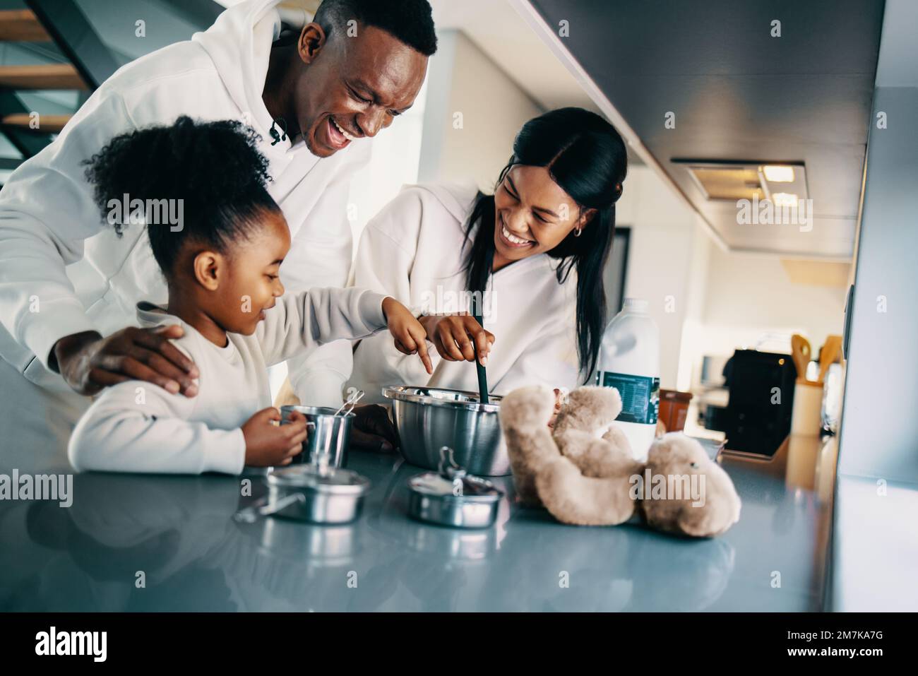 Zwei Eltern machen Pfannkuchen mit ihrer Tochter in der Küche. Die schwarze Familie sieht glücklich aus, wenn sie am Wochenende zusammen Frühstück zubereiten. Paar B. Stockfoto