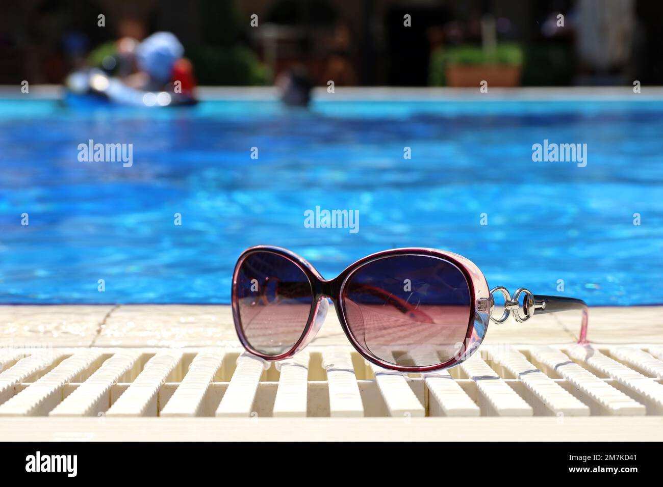 Sonnenbrille am Rand des Swimmingpools mit blauem Wasser. Sonniger Urlaub am Strandresort Stockfoto