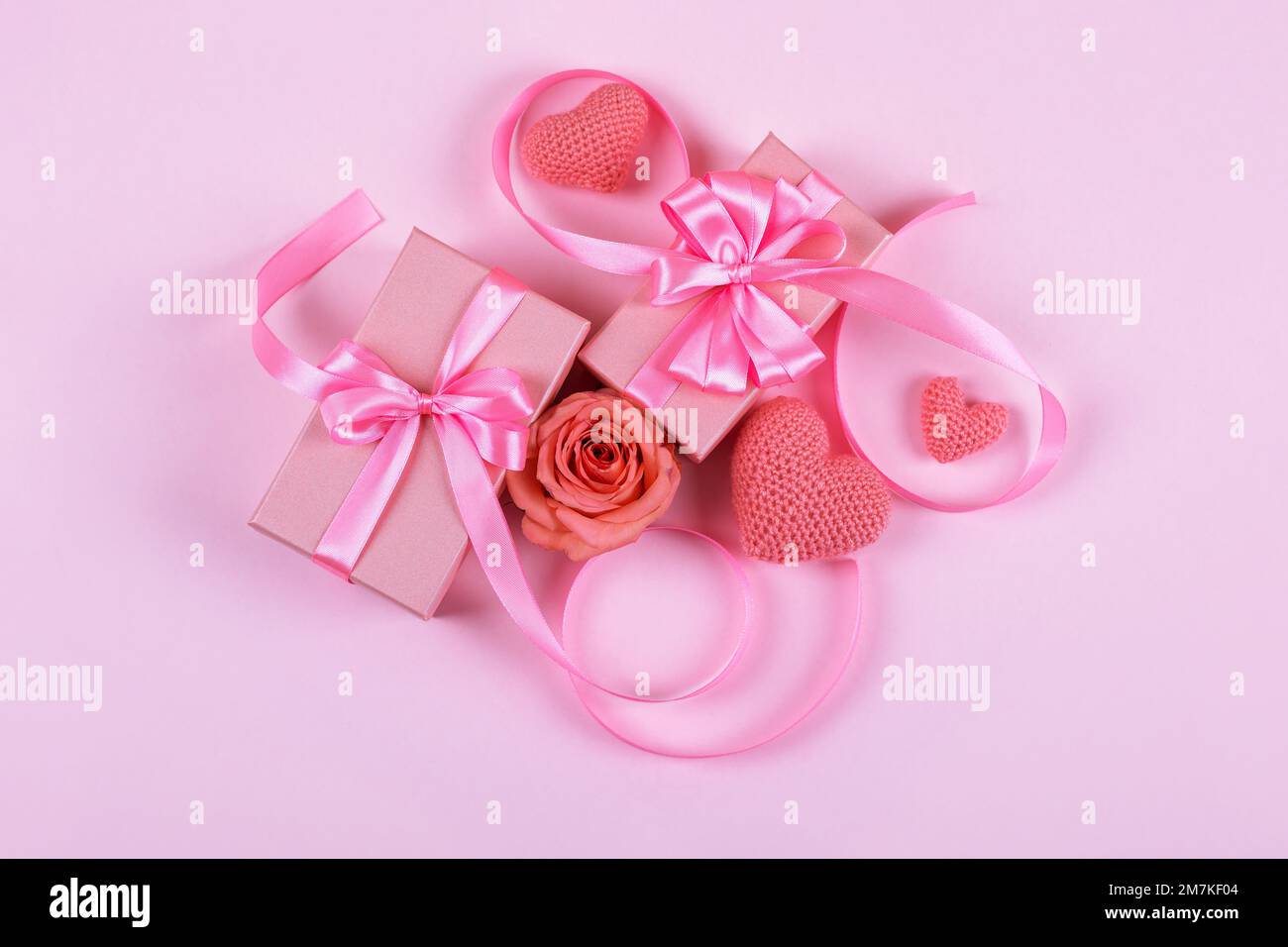Grußkarte zum Valentinstag, Muttertag und Geburtstag. Pinke Rosen, gestrickte pinke Herzen, Geschenkbox mit Satinschleife auf pinkfarbenem Hintergrund Stockfoto