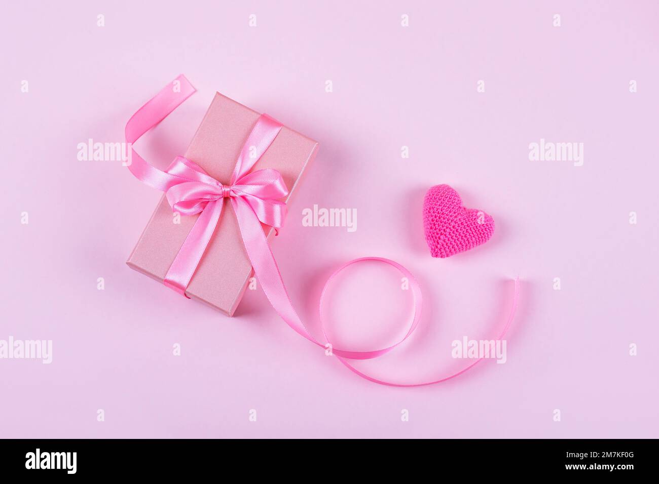 Grußkarte zum Valentinstag, Muttertag und Geburtstag. Gestricktes rosa Herz und Geschenkbox mit Schleife aus Satin auf pinkfarbenem Hintergrund Stockfoto
