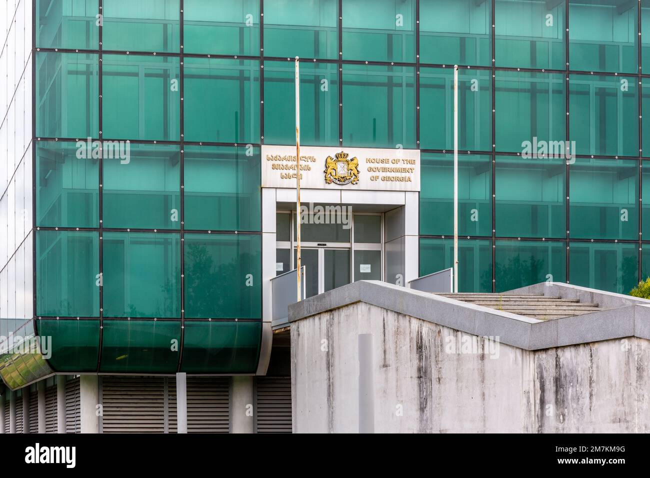 Kutaisi, Georgia, 06.06.21. Eingang zum Haus der Regierung von Georgien in Kutaisi, ein modernes, verlassenes Gebäude aus grünem Glas mit Wappen. Stockfoto