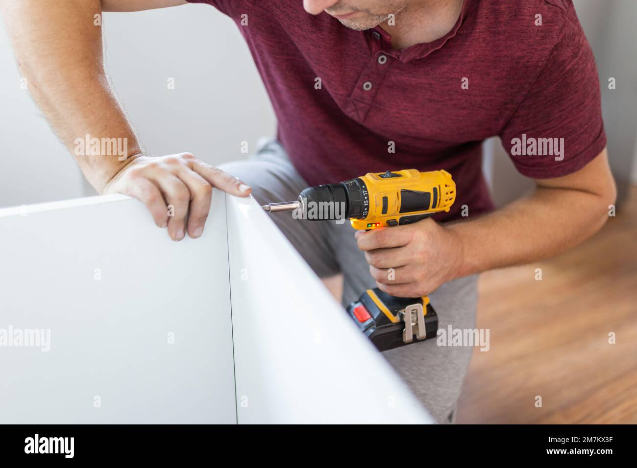 Nahaufnahme eines Mannes, der während der Installation von hölzernen Küchenregalen einen elektrischen Akkuschrauber hält Stockfoto