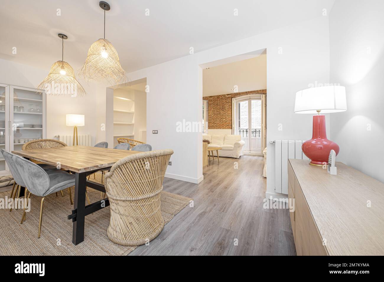 Wohnzimmer mit einem hölzernen Esstisch aus verklebten Brettern, mit hellblauem Samt gepolsterten Stühlen auf einem Gemüsefaserteppich und Zugang zu einem Zimmerwitze Stockfoto