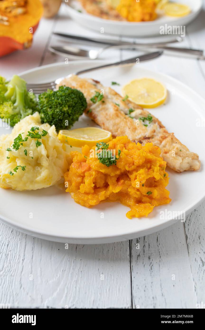Fischfilet mit Kartoffelpüree und rotem Kuri-Kürbispüree. Serviert mit Brokkoli auf einem Teller Stockfoto