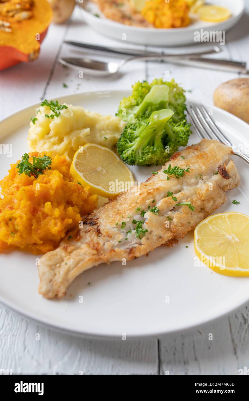 Gebratenes Fischfilet in der Pfanne mit Kartoffelpüree, Kürbispüree und Brokkoli auf einem Teller mit weißem Hintergrund Stockfoto