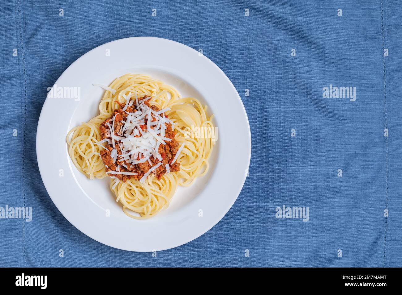 Bolognese-Spaghetti mit Parmesankäse auf weißem Teller. Einfacher blauer Hintergrund und Dekoration. Traditionelles italienisches Gericht, mediterrane Küche Stockfoto
