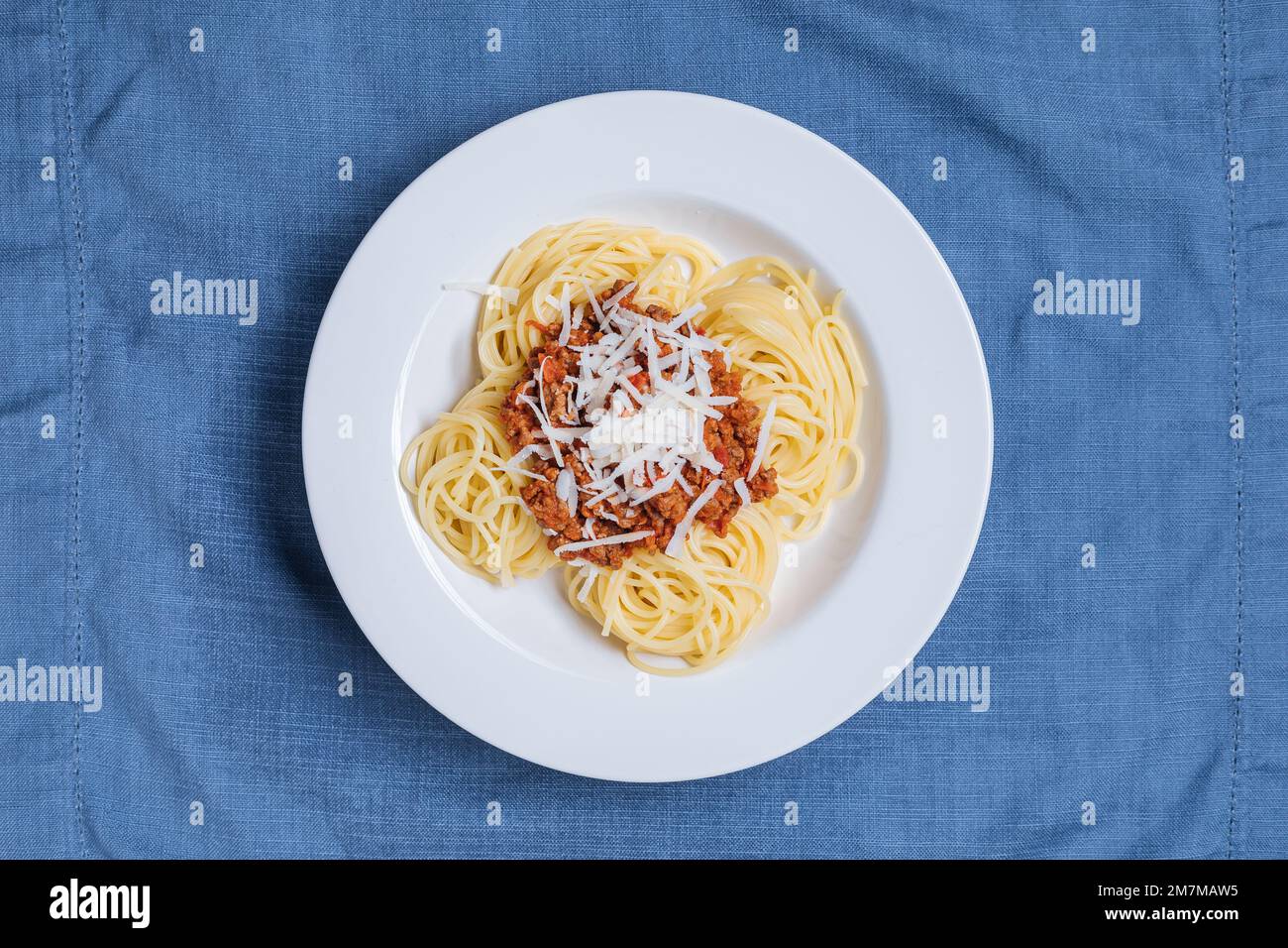Bolognese-Spaghetti mit Parmesankäse auf weißem Teller. Einfacher blauer Hintergrund und Dekoration. Traditionelles italienisches Gericht, mediterrane Küche Stockfoto