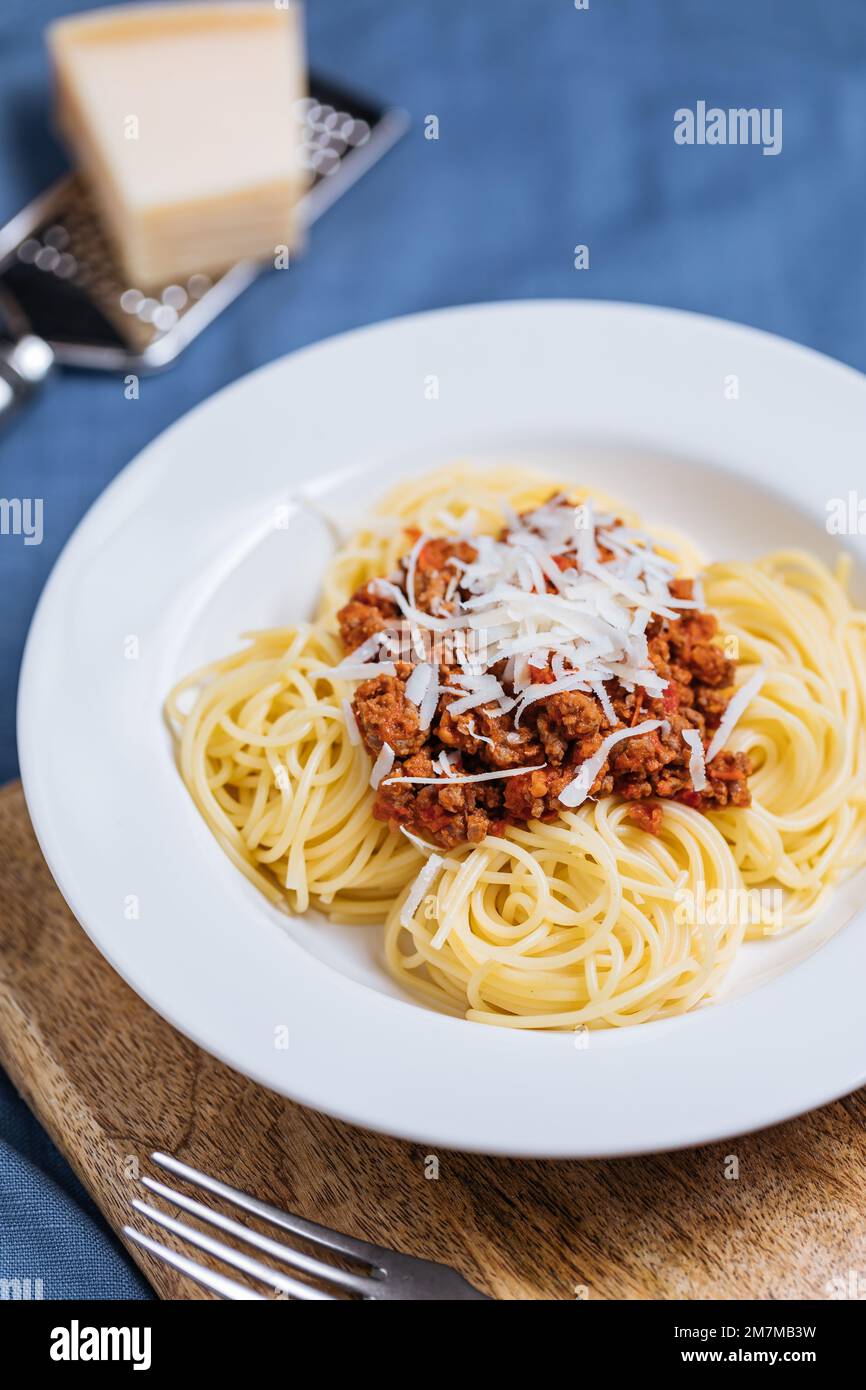 Bolognese-Spaghetti mit Parmesankäse auf weißem Teller. Einfacher blauer Hintergrund und Dekoration. Traditionelles italienisches Gericht, mediterrane Küche Stockfoto