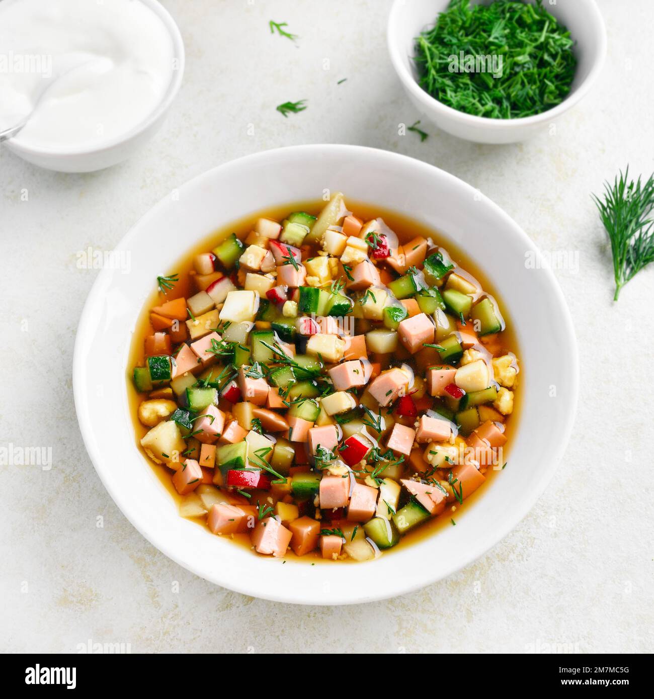 Kalte Sommer-Okroshka-Suppe mit Wurst, frischem Gemüse und Kvass in der Schüssel auf hellem Steinhintergrund. Nahaufnahme Stockfoto