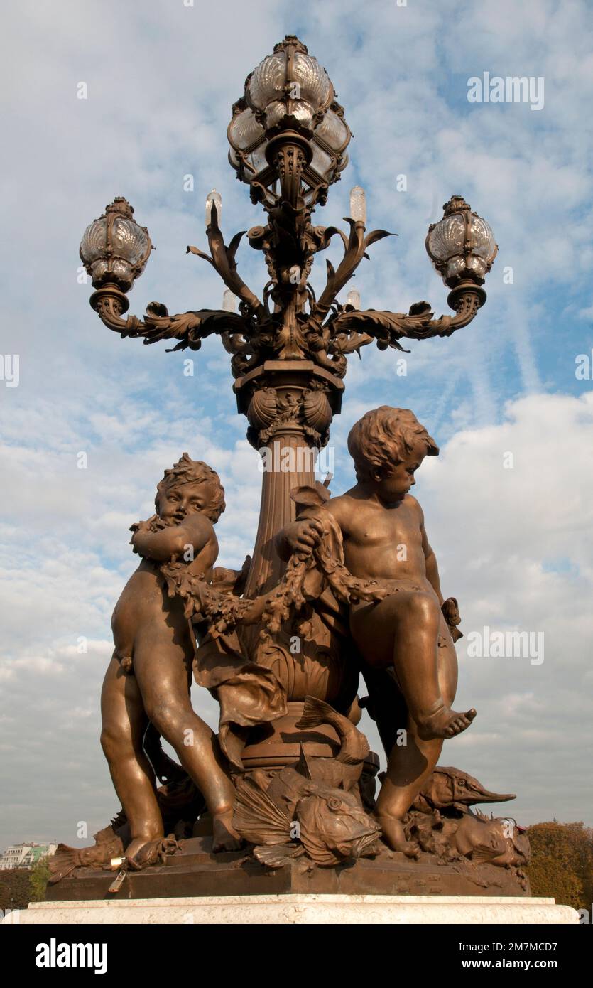 Bronzeskulpturen am Fuße einer kunstvoll verzierten Jugendstillampe auf der Pont Alexandre III Brücke in Paris. Stockfoto