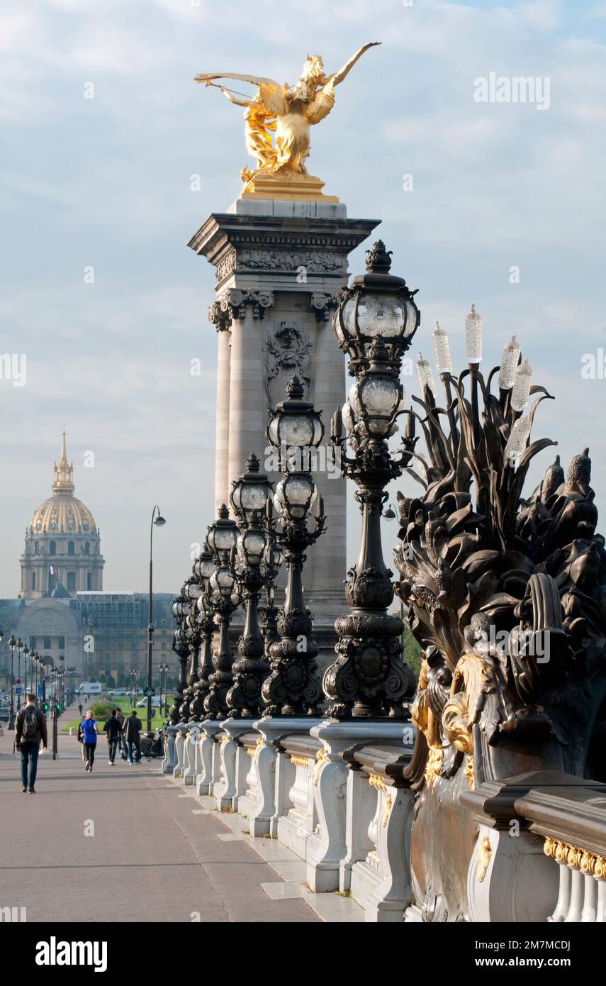Fußgänger gehen auf der prunkvollen Brücke Pont Alexandre III in Paris, mit dem Wahrzeichen Dôme des Invalides im Hintergrund. Stockfoto