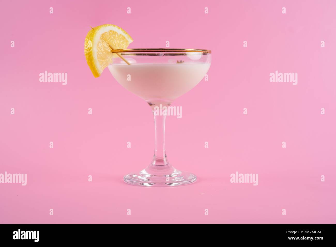 Frisch zubereiteter und gegossener Tuxedo-Cocktail mit einer Zitronenscheibe auf einem Kokosschwanz isoliert auf pinkfarbenem Hintergrund Stockfoto