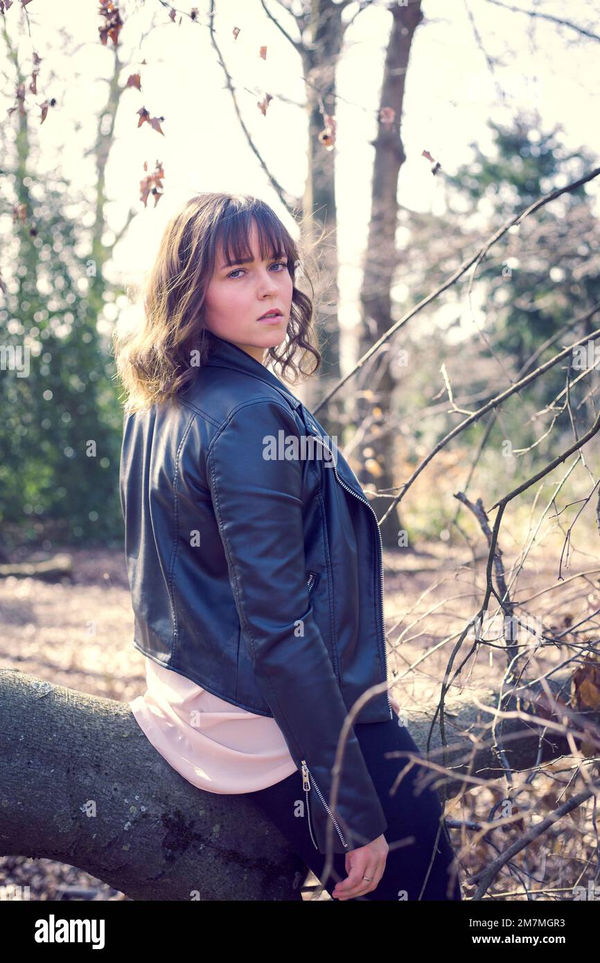 Junge Frau, die auf dem Baumstamm sitzt und über die Schulter in die Kamera schaut Stockfoto