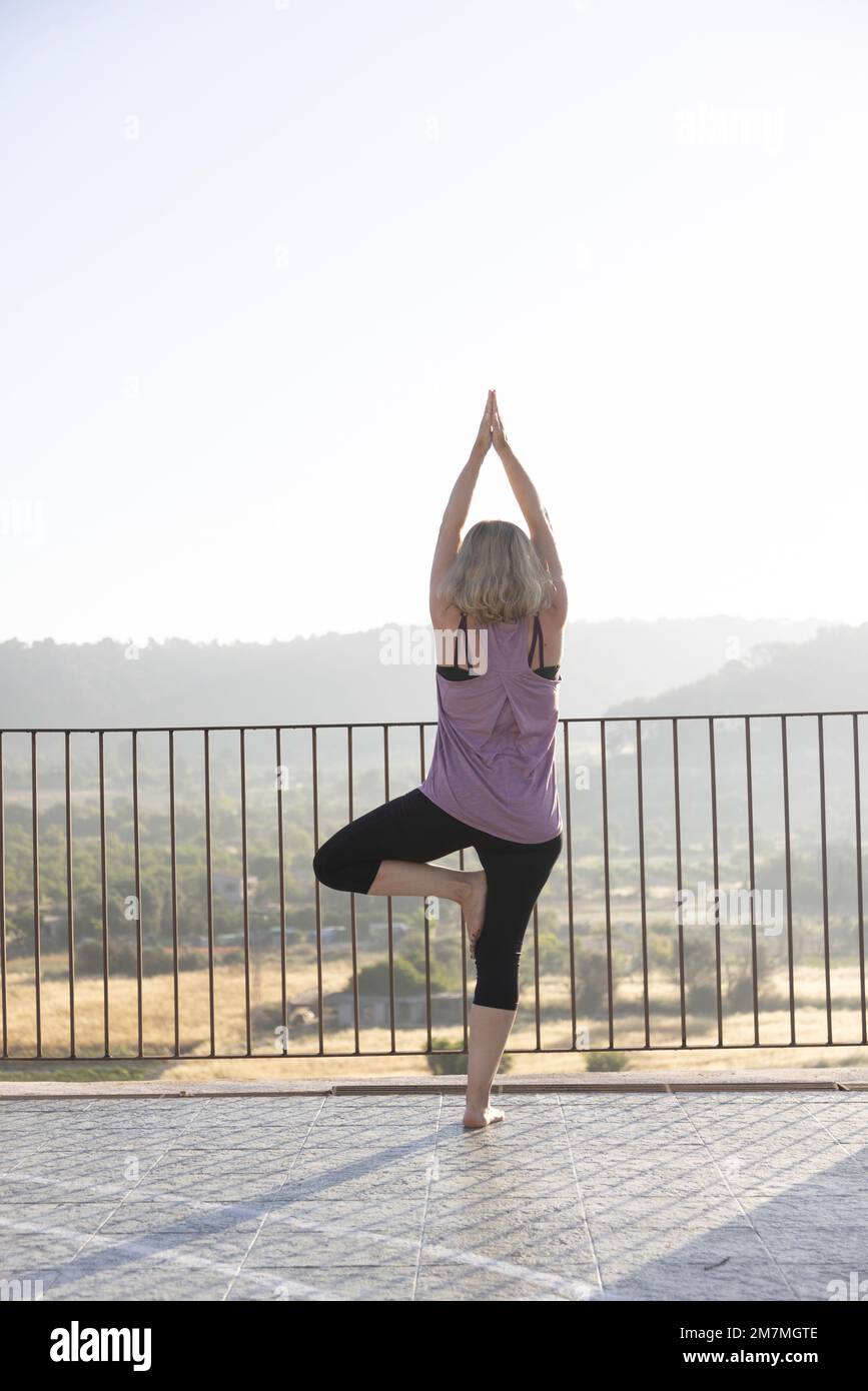 Blonde Frau, die bei Sonnenaufgang Yoga auf einer Terrasse in Spanien praktiziert Stockfoto