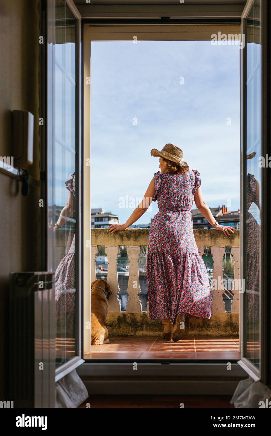 Stilvolle Frau, die die Aussicht genießt, während sie sich mit einem Hund auf dem Balkon entspannt. Stockfoto