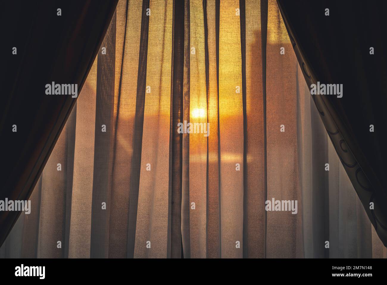 Sonnenaufgang, Blick durch den halbtransparenten Vorhang des Hotelzimmers, Hintergrundbeleuchtung, Silhouette der Stadt nur schwach sichtbar Stockfoto
