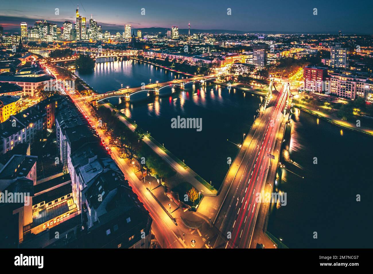 Blick von oben auf eine abendliche Stadt mit Fluss. Beleuchtete Straßen bei Sonnenuntergang, Lindnerhotel, Frankfurt am Main, Hessen, Deutschland Stockfoto