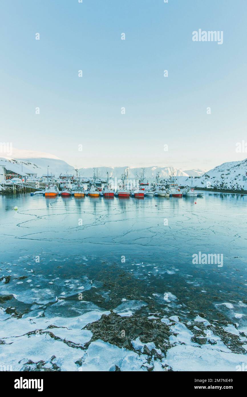 Fischerboote in einer Reihe an einem gefrorenen Fjord in Norwegen, Meer mit Schnee und Eis in einem Hafen, Landschaft in Skandinavien, Küstenregion Stockfoto