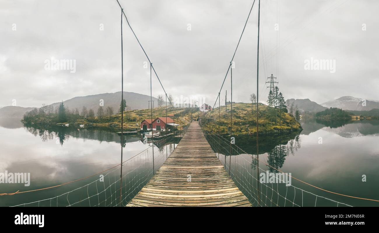 Alte hölzerne Hängebrücke im Fjord, Inselgruppen mit Fischerhütten, Häuser, Boote, Strommasten in Norwegen, Landschaft mit einsamem Fischerdorf, typische Fjordlandschaft mit kleinen Inseln, Skandinavien Stockfoto