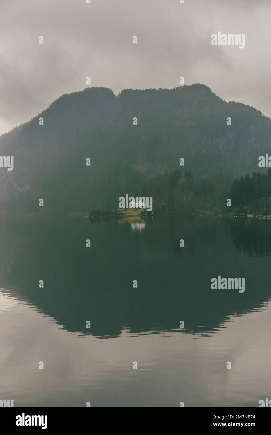 Einsames Haus auf einer Insel in Norwegen, Landschaft mit Reflexion im Wasser, typische Fjordlandschaft mit kleinen Inseln, Isolation von der Außenwelt, zentrale Perspektive Stockfoto