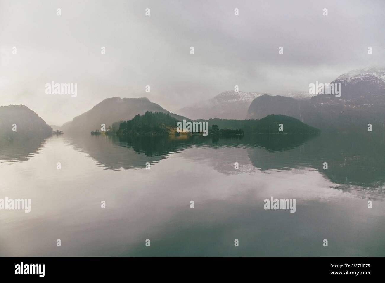 Einsame Häuser auf einer Insel in Norwegen, Landschaft mit Reflexion im Wasser, Nebel und Wolken, typische Fjordlandschaft mit kleinen Inseln, Abgeschiedenheit von der Außenwelt, zentrale Perspektive Stockfoto