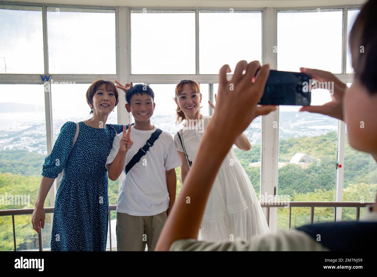 Ein Junge, der mit seinem Handy drei Personen fotografiert, einen 13-jährigen Jungen, seine Mutter und einen Freund. Stockfoto