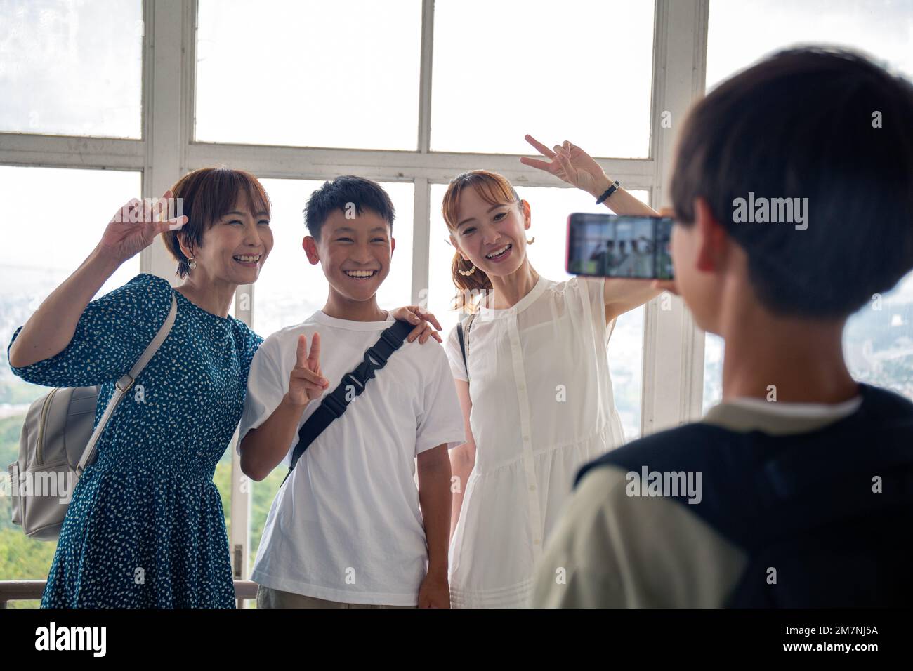 Ein Junge, der mit seinem Handy drei Japaner fotografiert, einen 13-jährigen Jungen, seine Mutter und einen Freund. Stockfoto