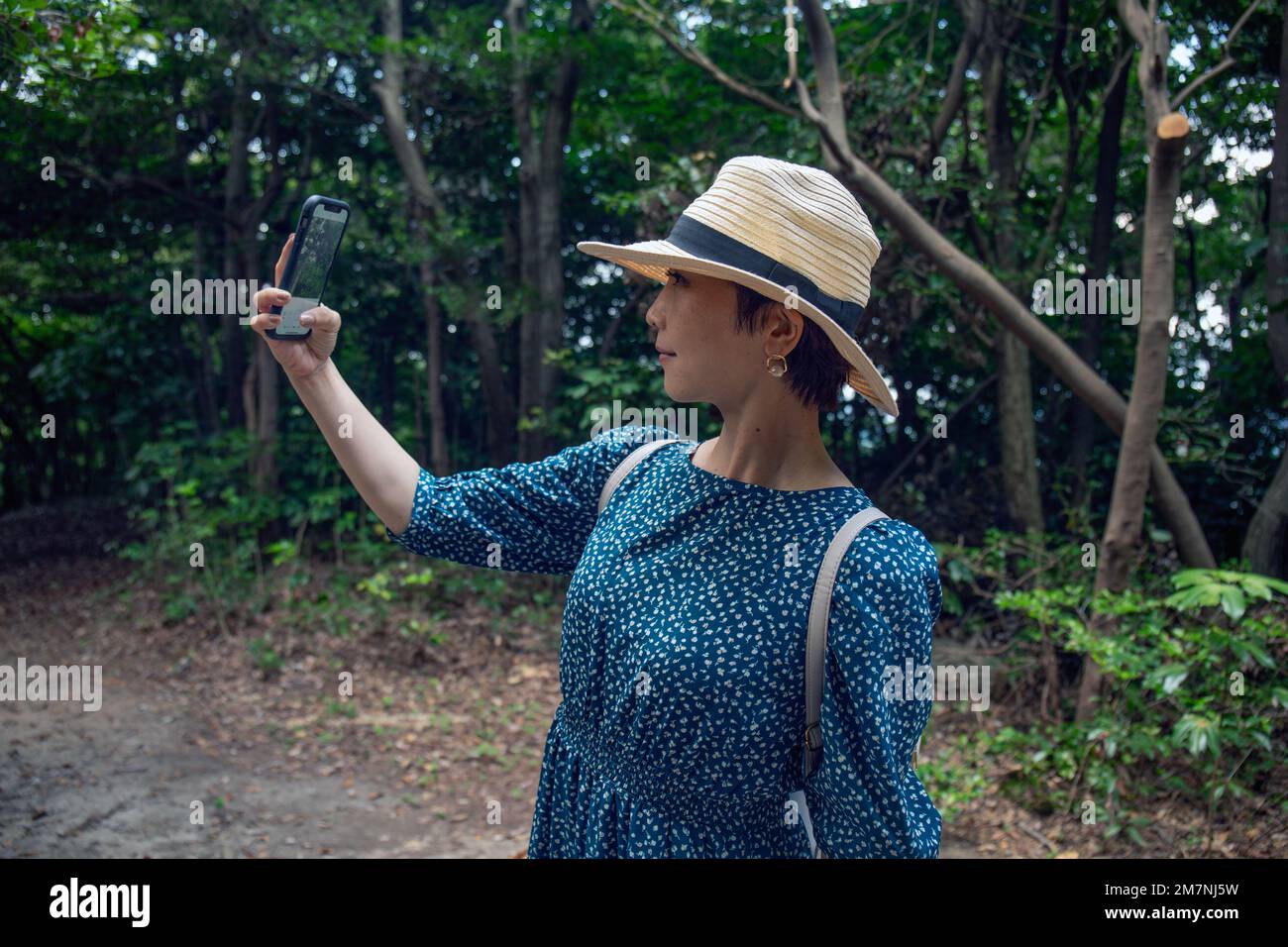 Eine reife Japanerin mit Strohhut und blauem Kleid, die ein Selfie mit einem Handy macht. Stockfoto