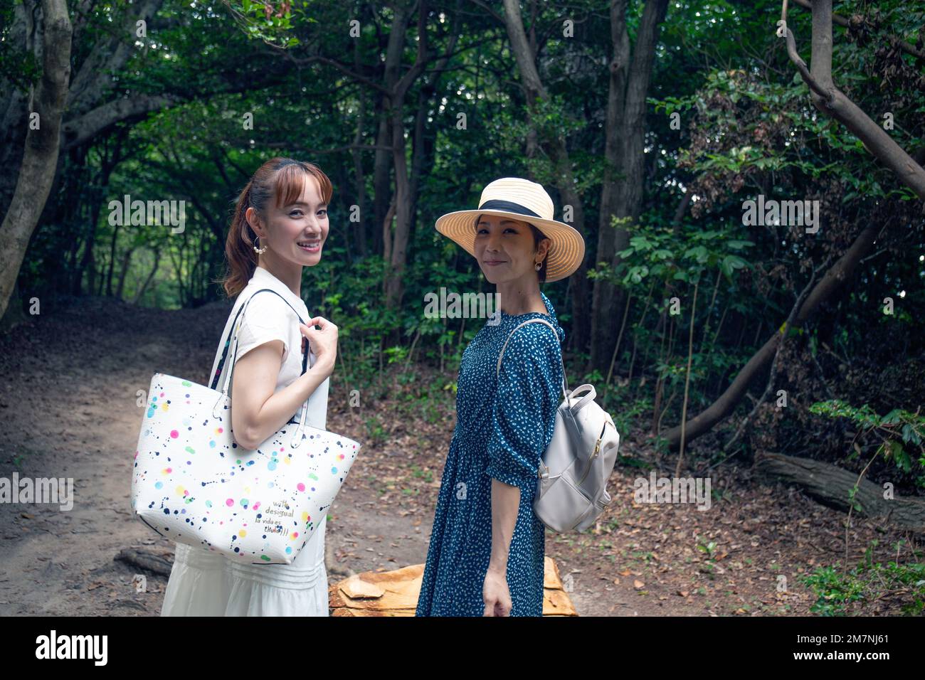 Zwei reife japanische Frauen in einem Park, die Taschen trugen, drehten sich an einem Tag die Köpfe um, um in die Kamera zu lächeln. Stockfoto