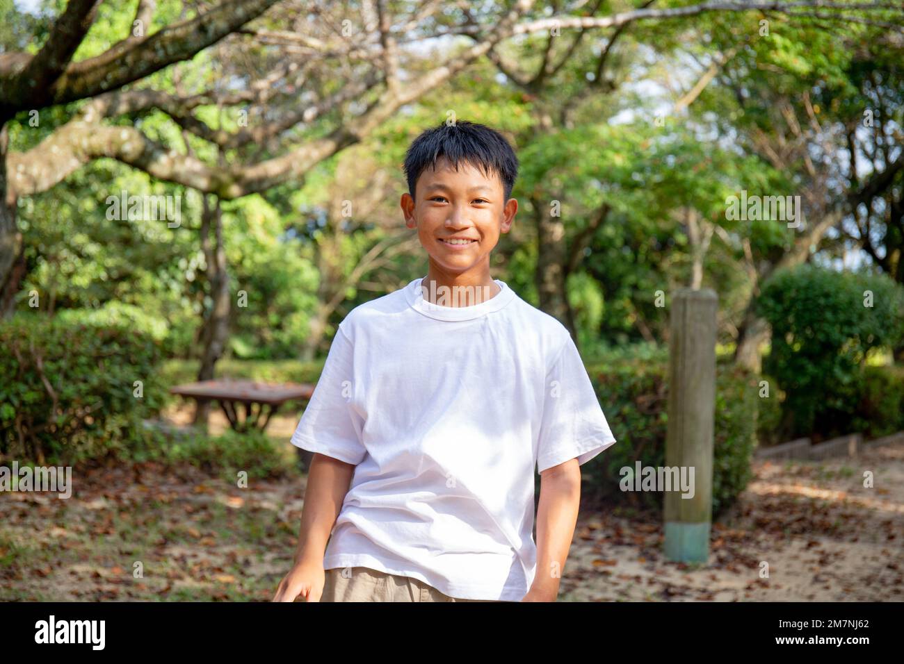 Ein 13-jähriger Junge in einem weißen teeshirt, lächelnd, draußen in einem Park. Stockfoto