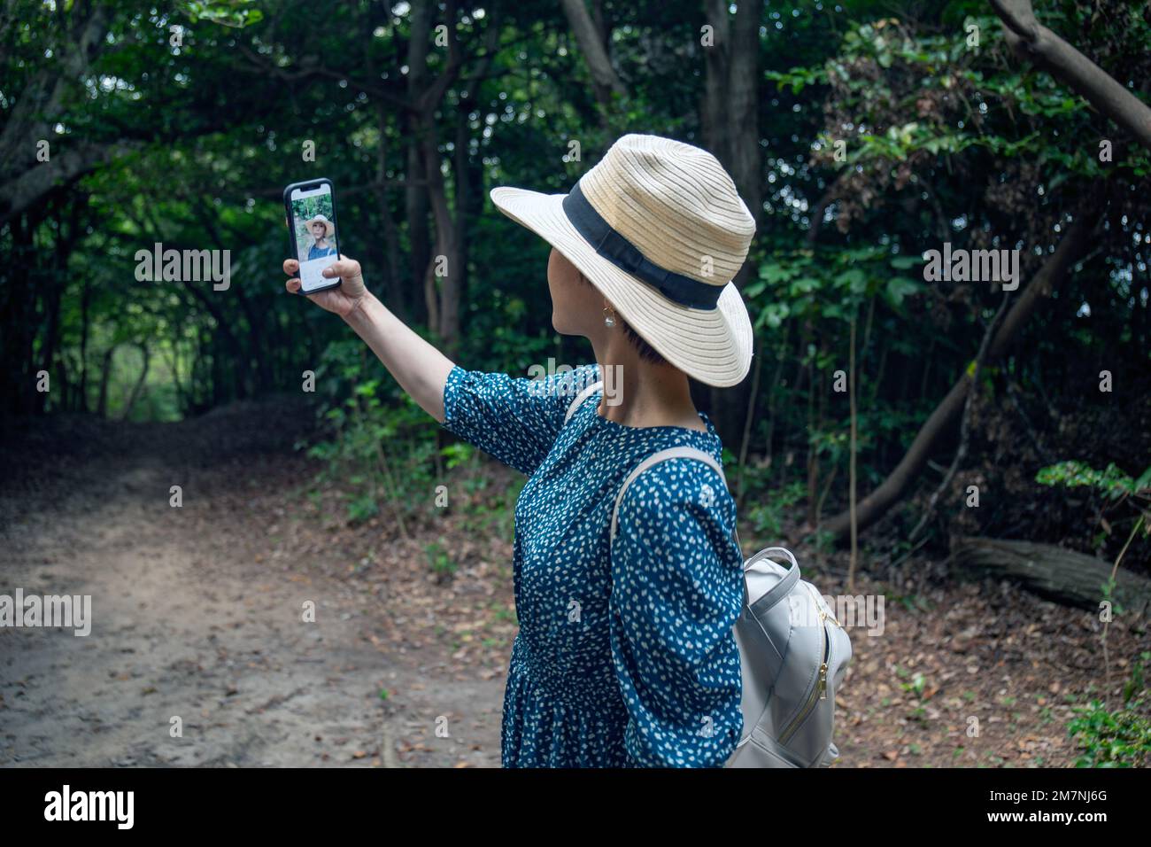 Eine reife Japanerin mit Strohhut und blauem Kleid, die ein Selfie mit einem Handy macht. Stockfoto