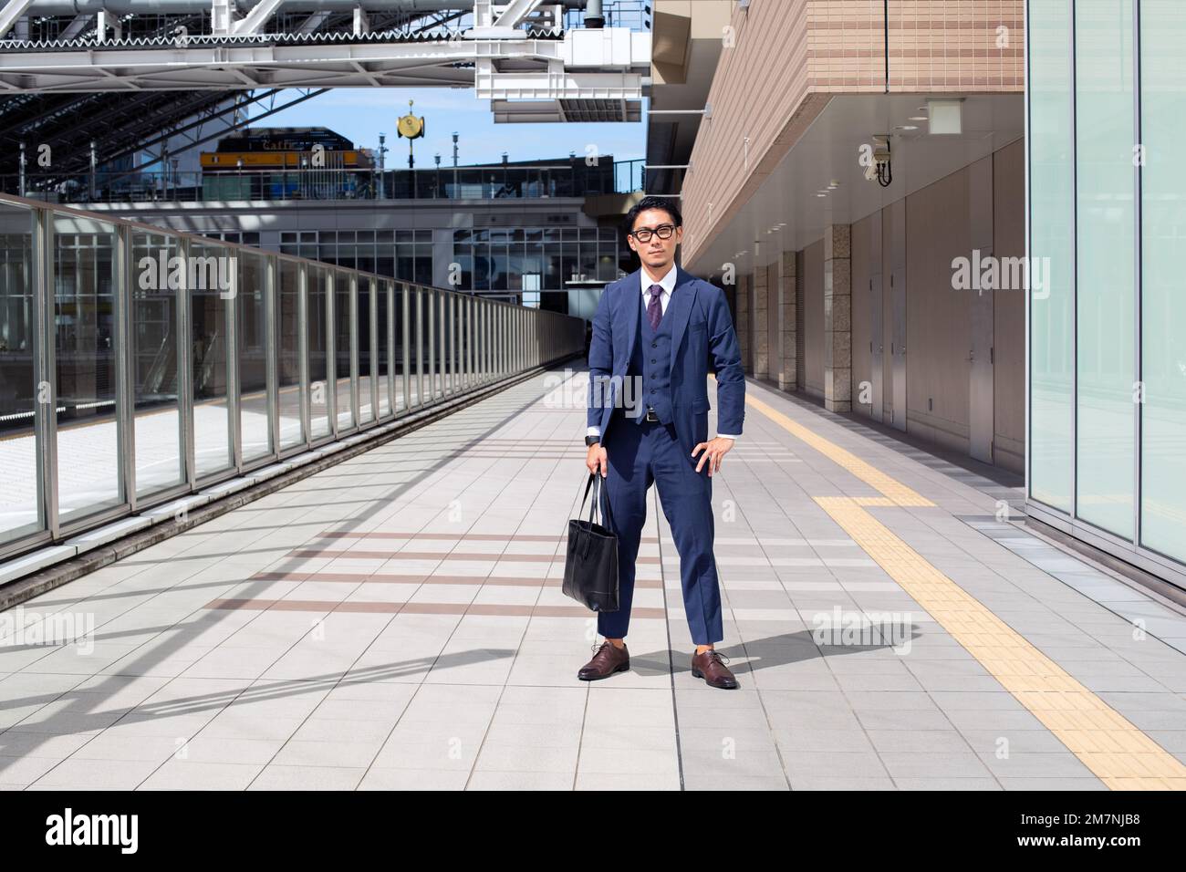 Ein junger Geschäftsmann in der Stadt, der unterwegs ist, ein Mann in einem Anzug mit einer Laptop-Tasche, der Beine auseinander auf einem Gehweg steht. Stockfoto
